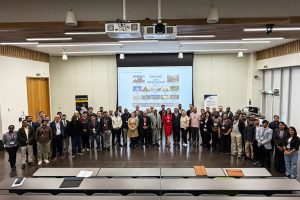Conference delegates gathered for a group photograph in lecture theatre, standing in front of presentation screen following an academic event.